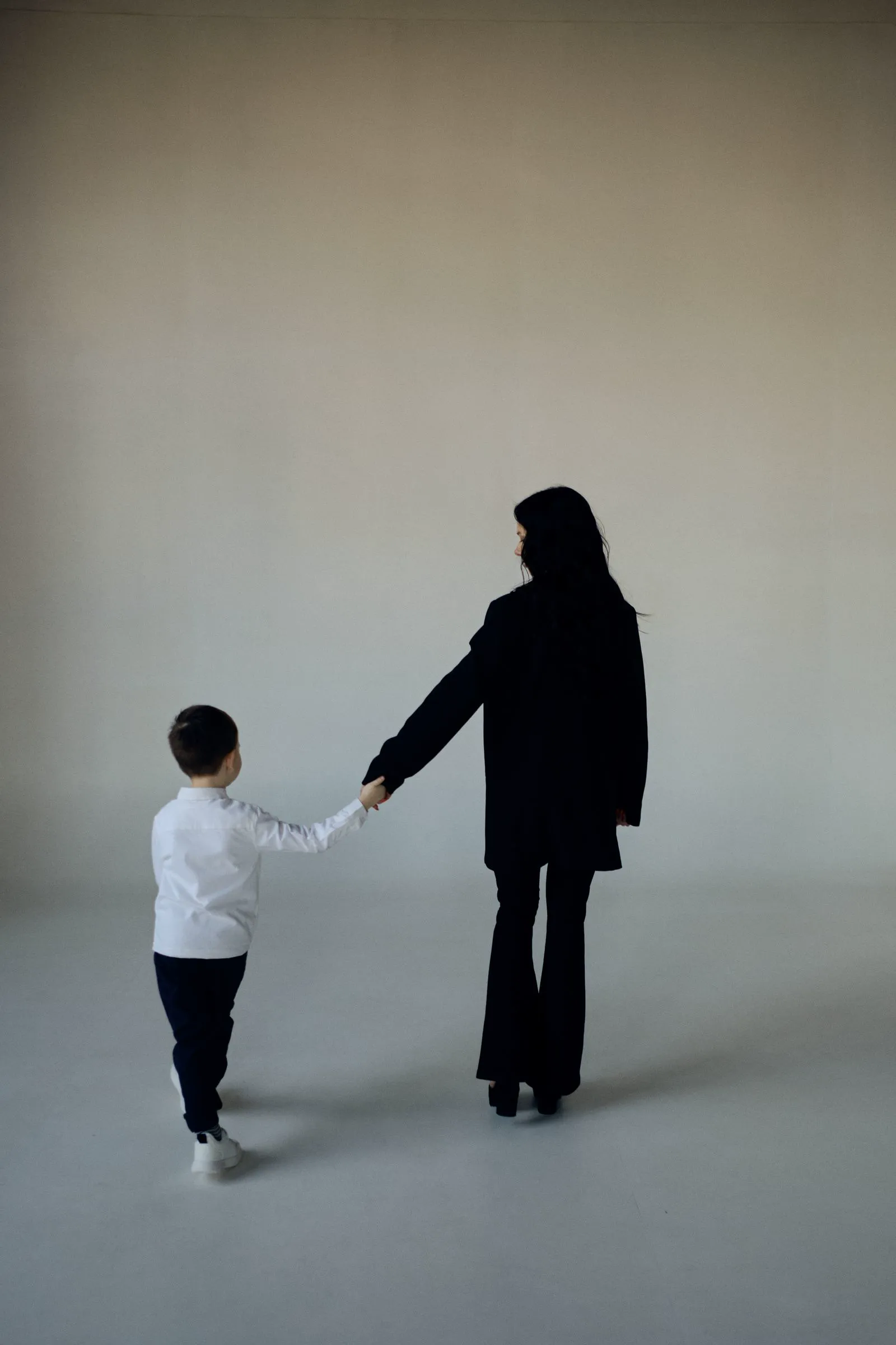 Mãe e filho de mãos dadas, vistos de costas